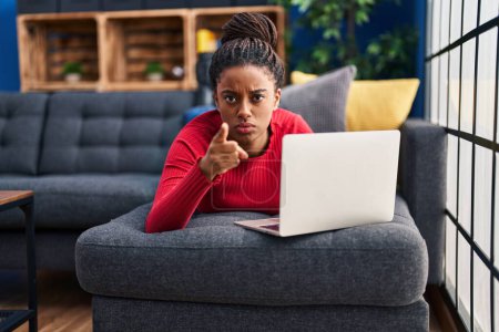 Photo for Young african american with braids working using computer laptop pointing with finger to the camera and to you, confident gesture looking serious - Royalty Free Image