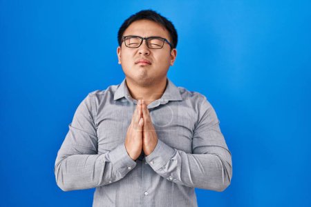 Photo for Young chinese man standing over blue background begging and praying with hands together with hope expression on face very emotional and worried. begging. - Royalty Free Image