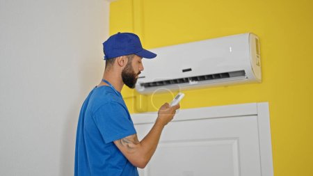 Téléchargez les photos : Jeune homme hispanique technicien réparer la machine de climatisation à l'aide de la télécommande à la maison - en image libre de droit