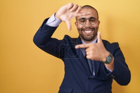 Téléchargez les photos : Homme hispanique avec barbe portant costume et cravate souriant faisant cadre avec les mains et les doigts avec le visage heureux. concept de créativité et photographie. - en image libre de droit