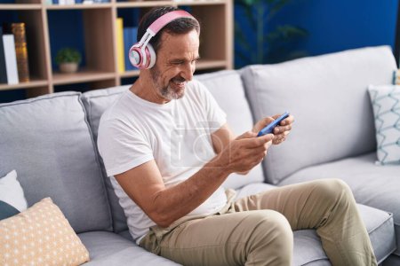 Photo for Middle age man playing video game sitting on sofa at home - Royalty Free Image