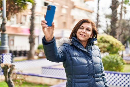 Photo for Middle age woman smiling confident making selfie by the smartphone at park - Royalty Free Image
