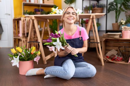 Foto de Joven mujer caucásica trabajando en floristería sentada de piso sonriendo y riendo en voz alta porque divertida broma loca. - Imagen libre de derechos