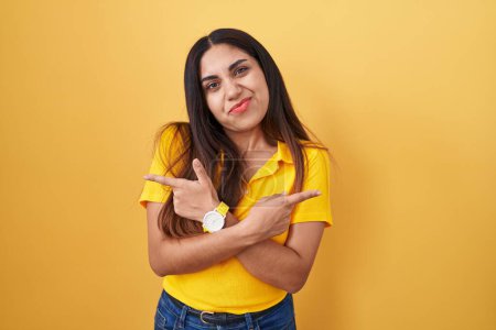 Téléchargez les photos : Jeune femme arabe debout sur fond jaune pointant des deux côtés avec les doigts, direction différente en désaccord - en image libre de droit