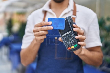 Young arab man waiter using data phone and credit card at restaurant