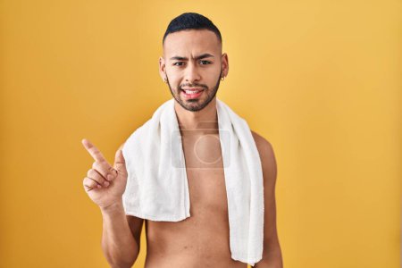 Photo for Young hispanic man standing shirtless with towel pointing aside worried and nervous with forefinger, concerned and surprised expression - Royalty Free Image