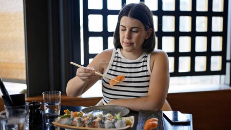 Téléchargez les photos : Jeune belle hispanique femme manger des sushis au restaurant - en image libre de droit