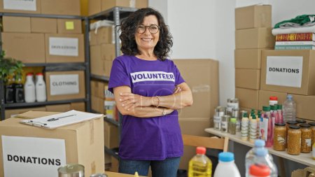 Photo for Middle age hispanic woman volunteer smiling confident standing with arms crossed gesture at charity center - Royalty Free Image