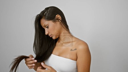 Téléchargez les photos : Jeune femme latine examinant les cheveux à la recherche bouleversée sur fond blanc isolé - en image libre de droit