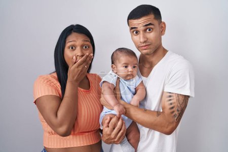 Photo for Young hispanic couple with baby standing together over isolated background shocked covering mouth with hands for mistake. secret concept. - Royalty Free Image
