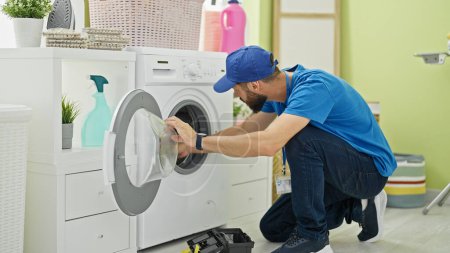 Téléchargez les photos : Jeune homme hispanique technicien réparation machine à laver à la buanderie - en image libre de droit