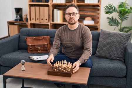 Photo for Middle age caucasian man playing chess sitting on the sofa thinking attitude and sober expression looking self confident - Royalty Free Image