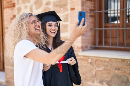 Photo for Two women mother and graduated daughter make selfie by smartphone at campus university - Royalty Free Image