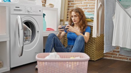 Photo for Young woman washing clothes playing video game at laundry room - Royalty Free Image