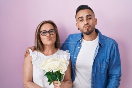 Photo for Hispanic mother and son together holding bouquet of white flowers looking at the camera blowing a kiss being lovely and sexy. love expression. - Royalty Free Image