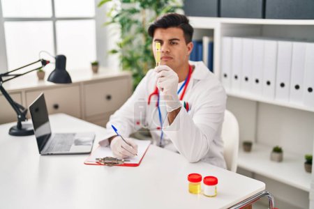 Photo for Young hispanic man doctor holding empty test tube at clinic - Royalty Free Image