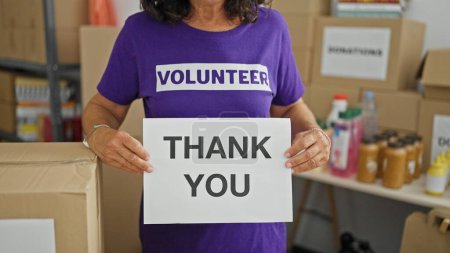 Foto de Mujer hispana de mediana edad voluntaria sosteniendo mensaje de agradecimiento en el centro de caridad - Imagen libre de derechos