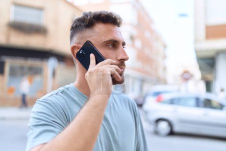 Téléchargez les photos : Jeune homme hispanique parlant sur smartphone avec une expression sérieuse dans la rue - en image libre de droit