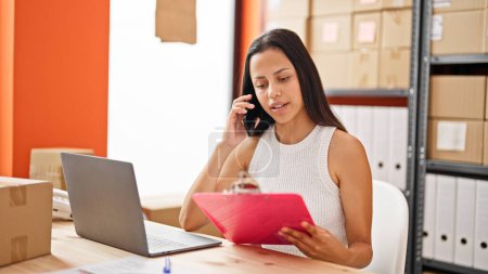Téléchargez les photos : Young beautiful hispanic woman ecommerce business worker talking on smartphone reading document at office - en image libre de droit
