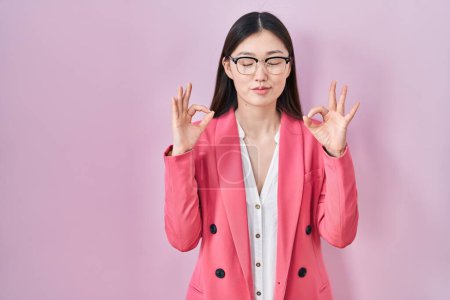 Photo for Chinese business young woman wearing glasses relax and smiling with eyes closed doing meditation gesture with fingers. yoga concept. - Royalty Free Image