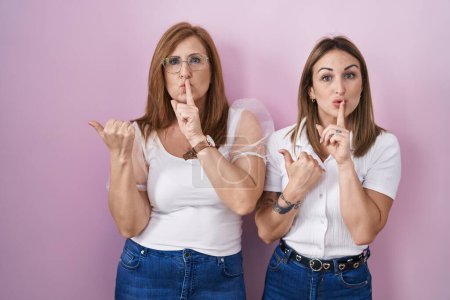 Téléchargez les photos : Mère et fille hispaniques portant un t-shirt blanc décontracté sur fond rose demandant de se taire avec le doigt sur les lèvres pointant avec la main sur le côté. silence et concept secret. - en image libre de droit