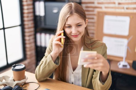 Foto de Mujer joven caucásica trabajadora de negocios hablando en teléfono inteligente recordatorio de lectura de papel en la oficina - Imagen libre de derechos