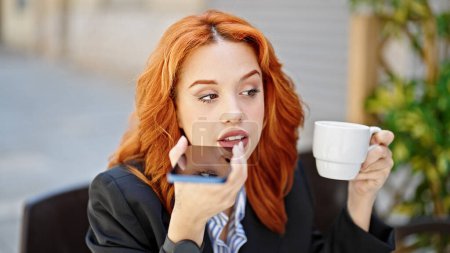 Téléchargez les photos : Jeune femme rousse d'affaires envoyant un message vocal par téléphone intelligent buvant du café sur la terrasse du café - en image libre de droit