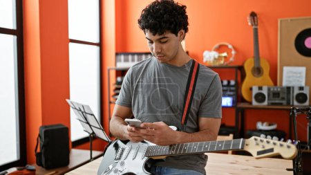 Téléchargez les photos : Jeune musicien latino-américain utilisant un smartphone au studio de musique - en image libre de droit