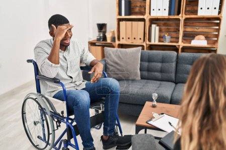 Photo for African american man doing therapy sitting on wheelchair very happy and smiling looking far away with hand over head. searching concept. - Royalty Free Image