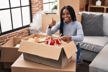 Foto de Mujer afroamericana mudándose a una nueva casa abriendo cajas sonriendo feliz y positivo, pulgar hacia arriba haciendo excelente y signo de aprobación - Imagen libre de derechos