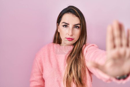Photo for Young hispanic woman standing over pink background doing stop sing with palm of the hand. warning expression with negative and serious gesture on the face. - Royalty Free Image