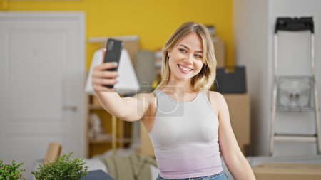 Téléchargez les photos : Jeune femme blonde faire selfie par smartphone debout à la nouvelle maison - en image libre de droit