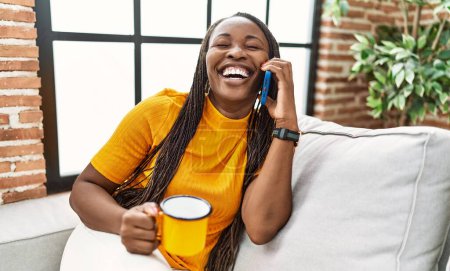 Téléchargez les photos : Femme afro-américaine parlant sur smartphone boire du café à la maison - en image libre de droit
