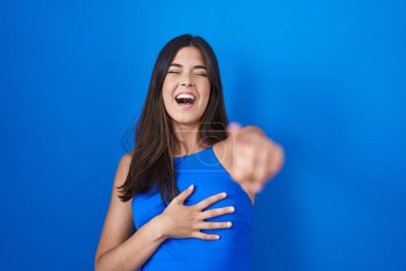 Téléchargez les photos : Femme hispanique debout sur fond bleu se moquant de vous, pointant du doigt la caméra avec la main sur le corps, expression de honte - en image libre de droit