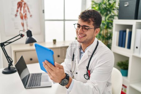 Photo for Young hispanic man doctor using laptop and touchpad working at clinic - Royalty Free Image