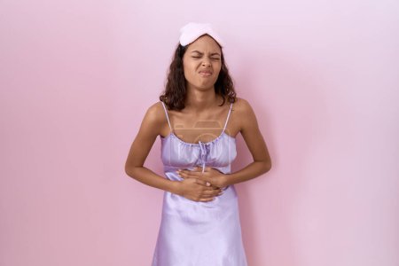 Photo for Young hispanic woman wearing sleep mask and nightgown with hand on stomach because indigestion, painful illness feeling unwell. ache concept. - Royalty Free Image