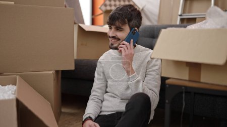 Téléchargez les photos : Jeune homme hispanique souriant confiant parler sur smartphone à la nouvelle maison - en image libre de droit