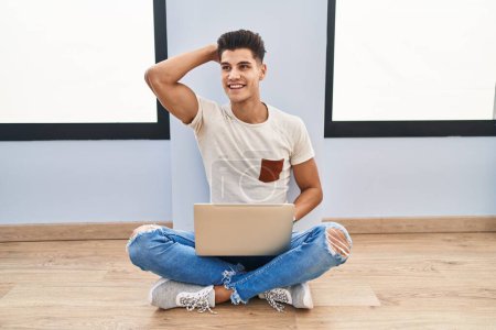 Téléchargez les photos : Jeune homme hispanique utilisant un ordinateur portable à la maison souriant confiant toucher les cheveux avec geste de la main vers le haut, posant attrayant et à la mode - en image libre de droit