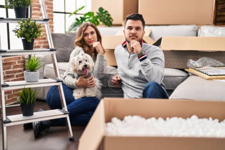 Photo for Young hispanic couple sitting on the floor at new home with log serious face thinking about question with hand on chin, thoughtful about confusing idea - Royalty Free Image