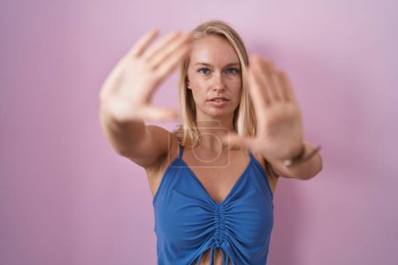 Foto de Joven mujer caucásica de pie sobre fondo rosa haciendo marco usando las manos palmas y los dedos, perspectiva de la cámara - Imagen libre de derechos