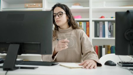 Téléchargez les photos : Jeune belle étudiante hispanique utilisant l'ordinateur prenant des notes à l'université de la bibliothèque - en image libre de droit