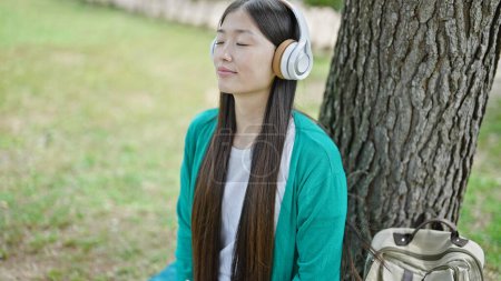 Téléchargez les photos : Jeune femme chinoise écoutant de la musique détendue au parc - en image libre de droit