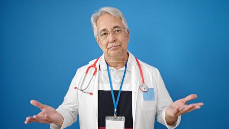 Photo for Middle age man with grey hair doctor standing clueless over isolated blue background - Royalty Free Image