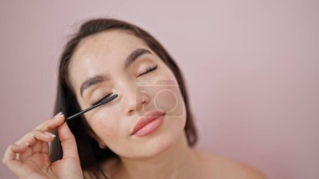 Téléchargez les photos : Jeune belle femme hispanique appliquant maquillage sur cils sur fond rose isolé - en image libre de droit