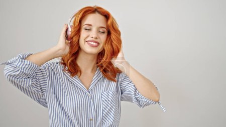 Téléchargez les photos : Jeune rousse femme écoutant de la musique souriant sur fond blanc isolé - en image libre de droit