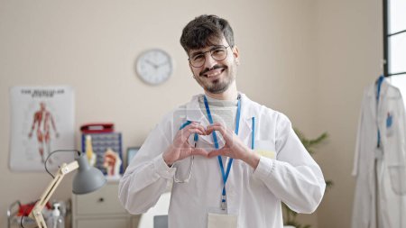 Photo for Young hispanic man doctor smiling doing heart gesture with hands at clinic - Royalty Free Image