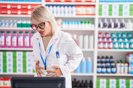 Téléchargez les photos : Young caucasian woman working at pharmacy drugstore with hand on stomach because indigestion, painful illness feeling unwell. ache concept. - en image libre de droit