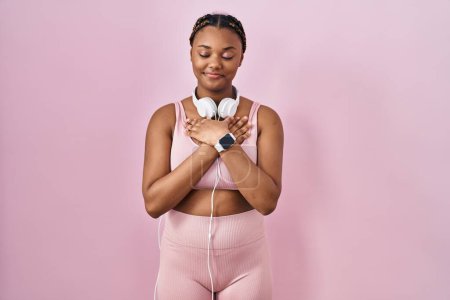 Photo for African american woman with braids wearing sportswear and headphones smiling with hands on chest with closed eyes and grateful gesture on face. health concept. - Royalty Free Image