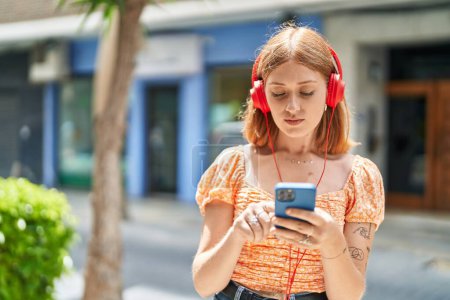 Téléchargez les photos : Jeune rousse femme écouter de la musique à la rue - en image libre de droit