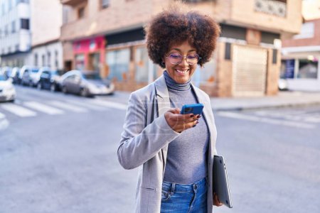 Téléchargez les photos : Afro-américaine femme exécutif en utilisant smartphone tenant ordinateur portable à la rue - en image libre de droit